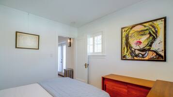 A bedroom with a bed, a wooden dresser, a painting, and a door leading to another room.