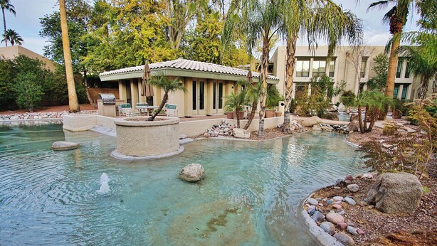 A pool area with a small waterfall, surrounded by rocks and palm trees. - Walk to Fashion Park! Phoenix Abode w/ Pool Access (Phoenix)