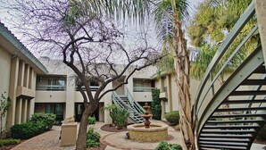 A courtyard with a central fountain, surrounded by a brick pathway and greenery, leading to a building with a spiral staircase. - Walk to Fashion Park! Phoenix Abode w/ Pool Access (Phoenix)