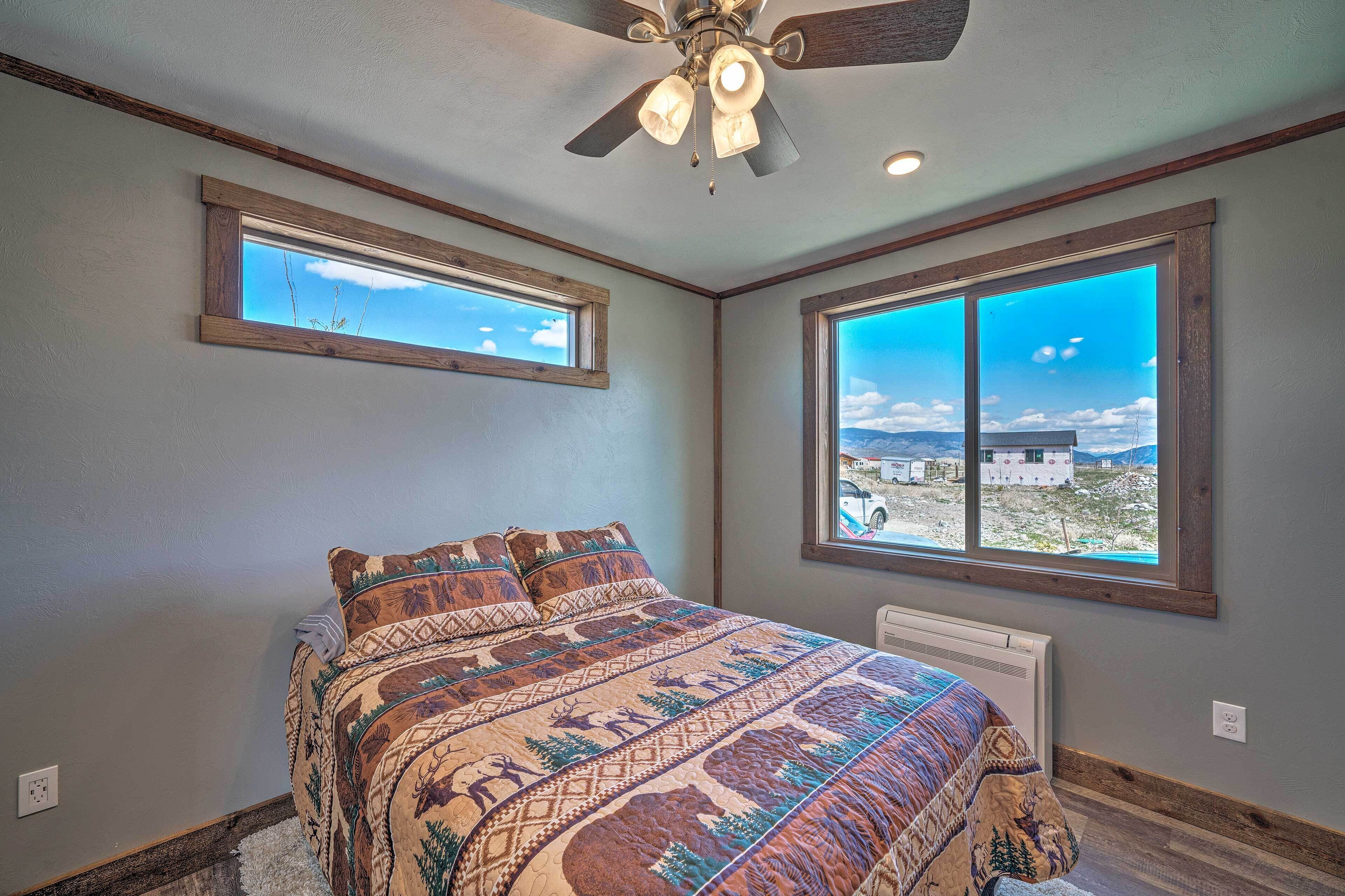 A bedroom with a large bed, two windows with views, a ceiling fan, and a radiator.
