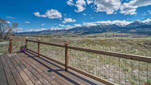 A wooden deck with a metal railing overlooking a mountainous landscape.