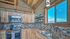 A kitchen with wooden cabinets, a stainless steel sink, and a large window offering a view of the sky.