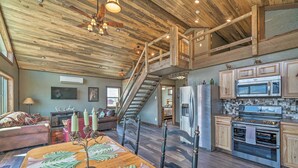 A spacious living area with a wooden ceiling, a staircase, a kitchen with modern appliances, and a cozy seating area.