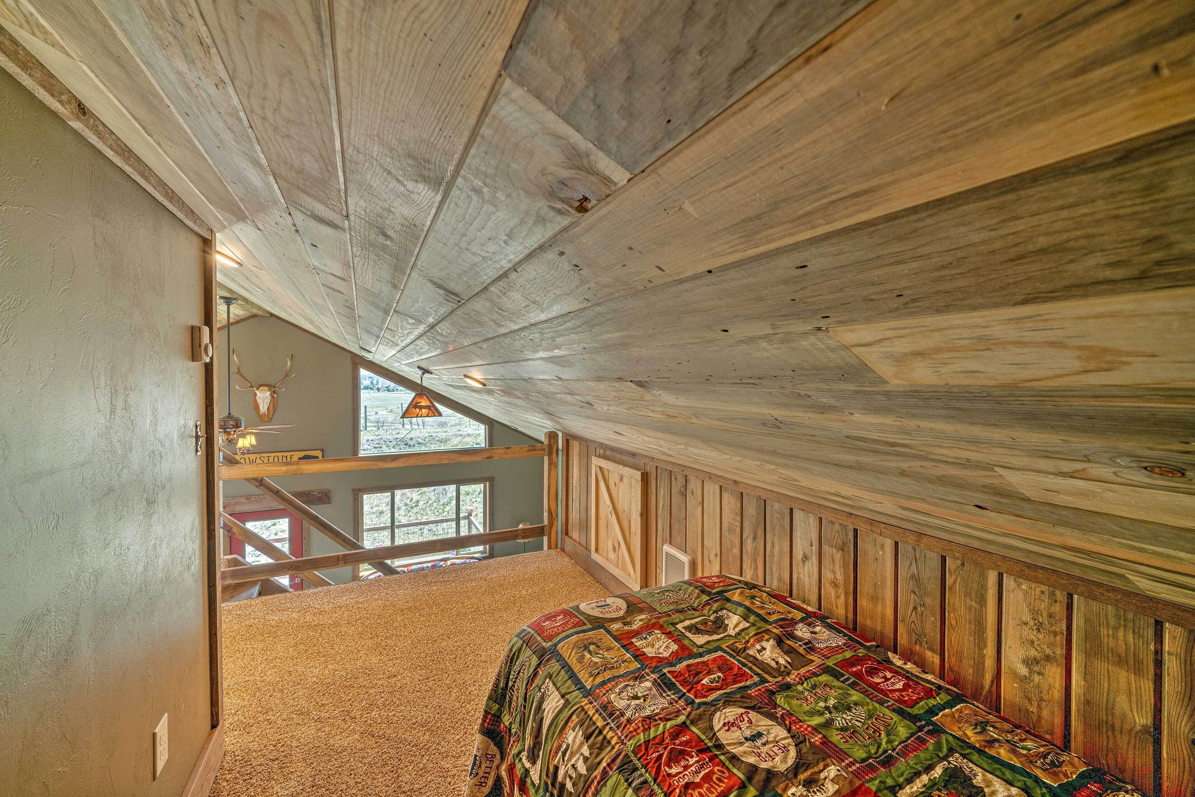 Quarto com teto de madeira, cama com colcha e vista para o exterior através de uma janela.