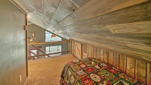 A bedroom with a wooden ceiling, a bed with a quilt, and a view of the outside through a window.