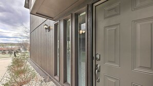 A building with a large gray door, a small window with a light fixture, and a pathway with gravel and shrubs.