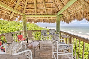 A covered outdoor seating area with wicker furniture and a thatched roof, overlooking a beach. - Jensen Beach Home: Walk to Beach Access! (Jensen Beach)
