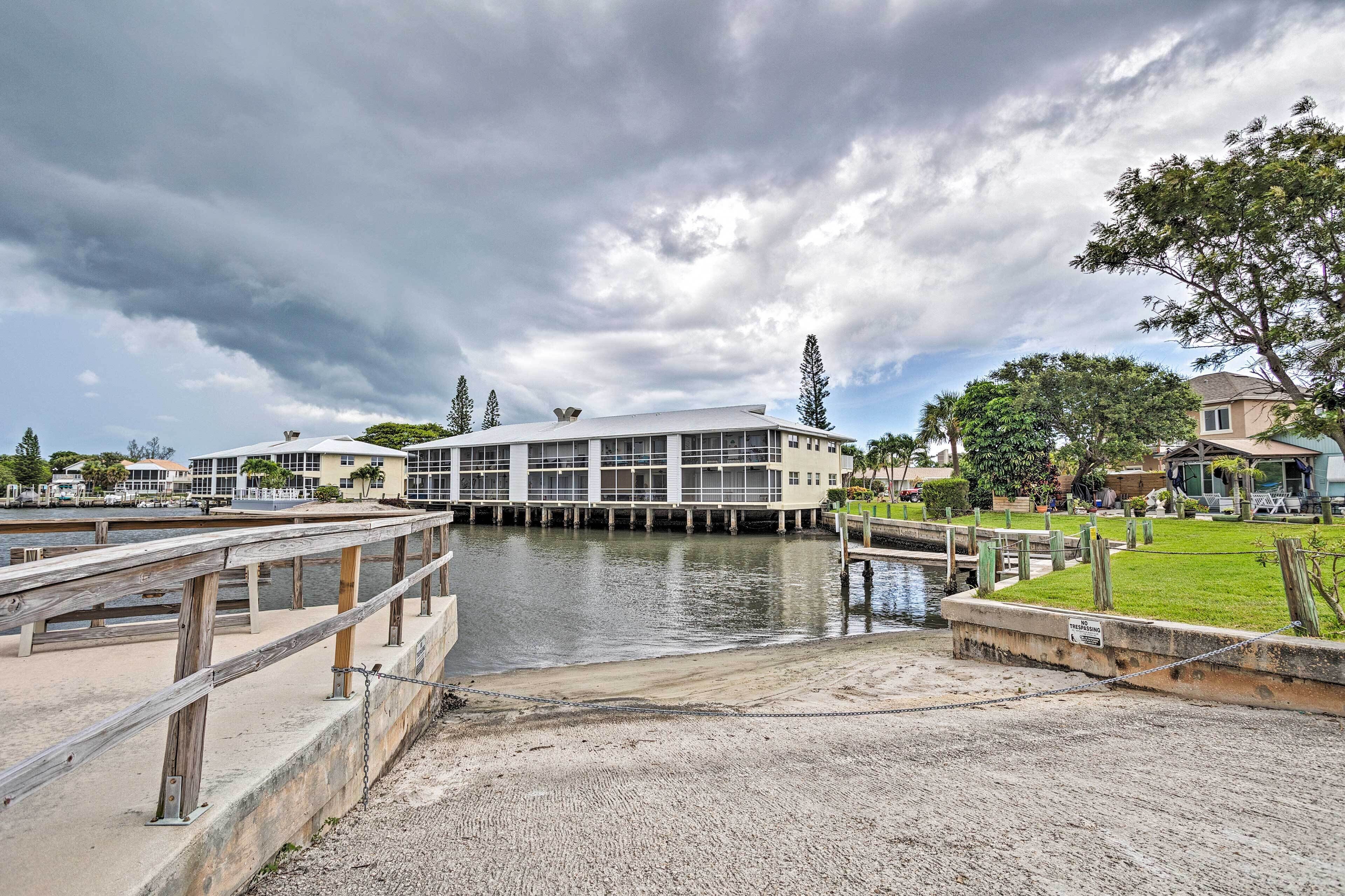 A waterfront building with a dock, surrounded by greenery and other buildings.