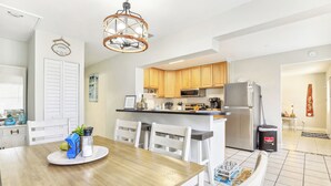 A modern kitchen with wooden cabinets, stainless steel appliances, and a dining area with a wooden table and white chairs. - Jensen Beach Home: Walk to Beach Access! (Jensen Beach)