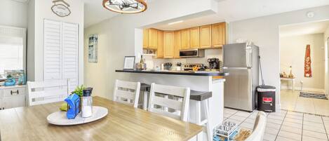 A modern kitchen with wooden cabinets, stainless steel appliances, and a dining area with a wooden table and white chairs.