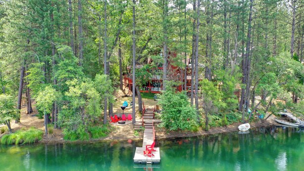 Uma cabana rodeada por uma floresta, um píer que se estende sobre um lago e um pequeno barco.