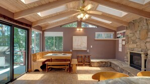 Um quarto espaçoso com teto alto, vigas de madeira, lareira de pedra e um espaço de jantar com bancos.