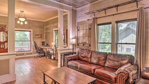 A spacious living room with a leather sofa, wooden flooring, and large windows. - Country-chic Cotter Home w/ Outdoor Living Space! (Cotter)