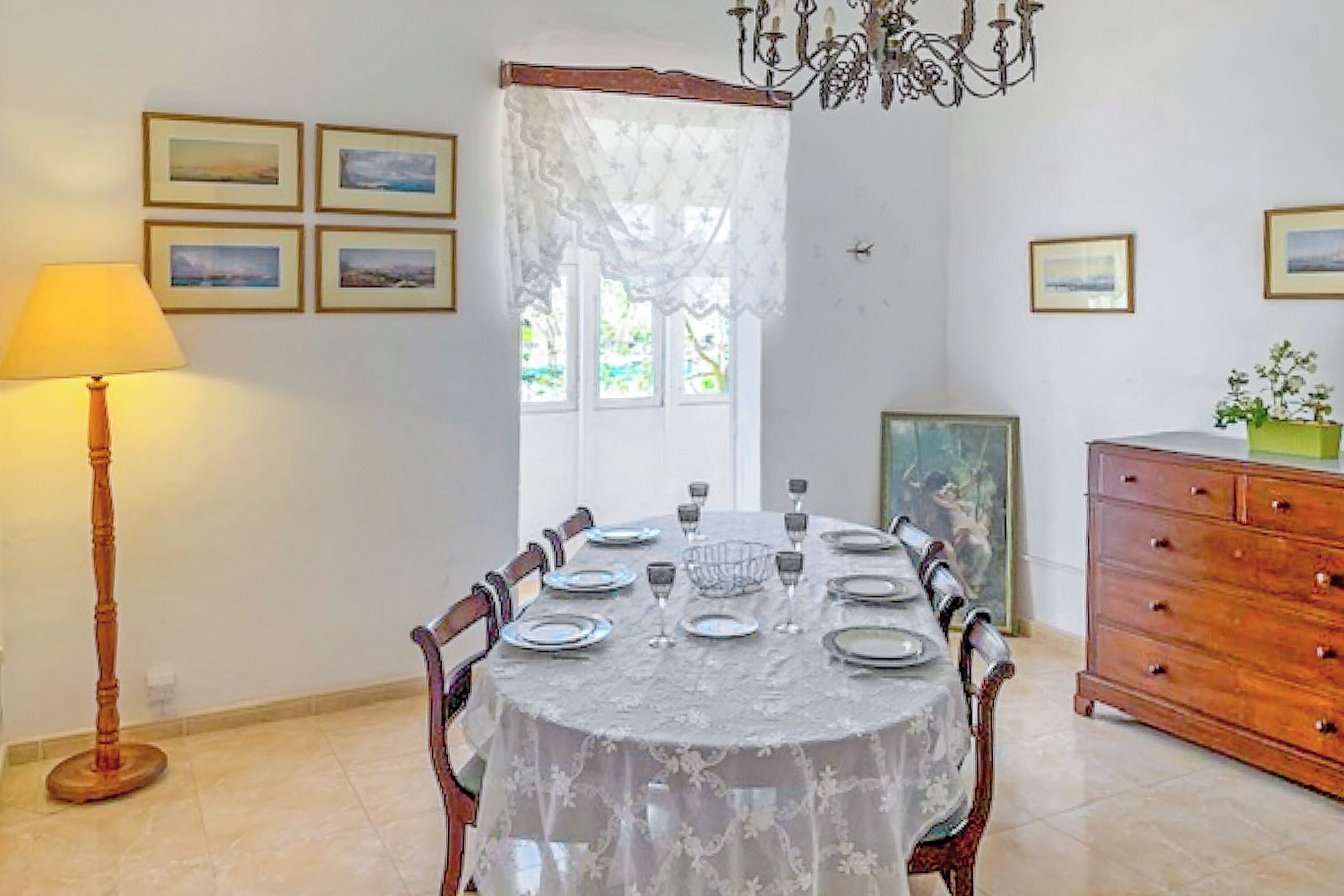 A dining area with a round table set for six, surrounded by chairs, a wooden cabinet, and a floor lamp.