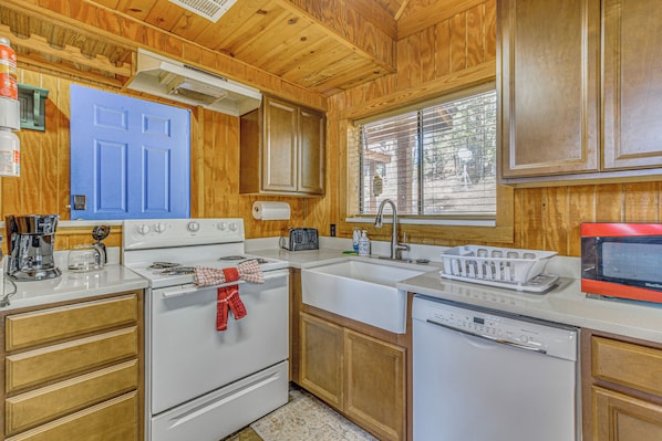 A kitchen with wooden cabinets, a blue door, a white stove, a sink, and a dishwasher.