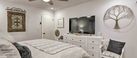 A bedroom with a bed, a chair, a dresser, a television, and a ceiling fan.