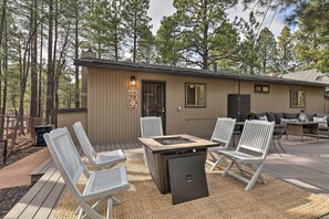 A wooden deck with a built-in fire pit and white chairs, surrounded by trees. - Renovated Cottage w/ Fire Pit in Munds Park! (Munds Park)