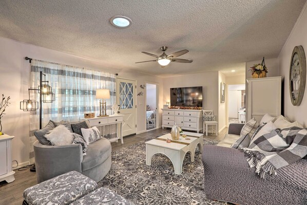 A living room with a sofa, armchair, coffee table, and a TV. There is a ceiling fan and a window with curtains. - Renovated Cottage w/ Fire Pit in Munds Park! (Munds Park)