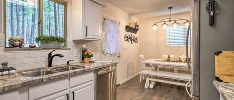 A modern kitchen with white cabinets, a stainless steel dishwasher, and a dining area with a bench and table.