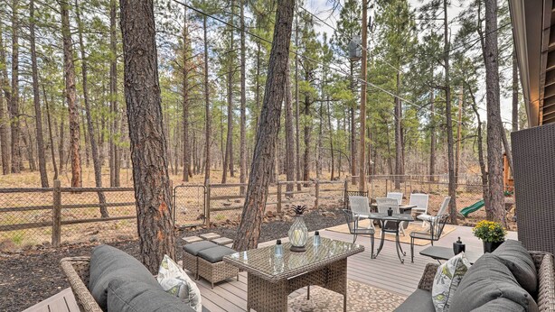 En terrasse med fletmøbler, et bord med glasplade og udsigt til en skov.