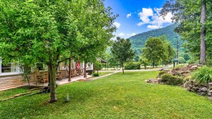 A lush green landscape with a stone building, a wooden deck, and a clear view of a mountain range. - Great Smoky Mountains Retreat w/ Fire Pit & Views! (Sevierville)