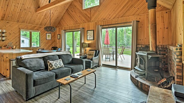 A cozy cabin interior with a wooden ceiling, a fireplace, a sofa, a coffee table, and a dining area. - Near Snowmobiling! Riverfront Traverse City Cabin (Traverse City)