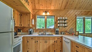 A wooden cabin kitchen with a central island, wooden cabinets, a sink, and a coffee maker. - Near Snowmobiling! Riverfront Traverse City Cabin (Traverse City)