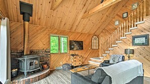 A cozy wooden cabin interior with a fireplace, a sofa, a coffee table, and a staircase. - Near Snowmobiling! Riverfront Traverse City Cabin (Traverse City)