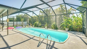 Une piscine extérieure couverte, dotée d’un toit en verre, entourée de verdure et agrémentée d’un espace patio.