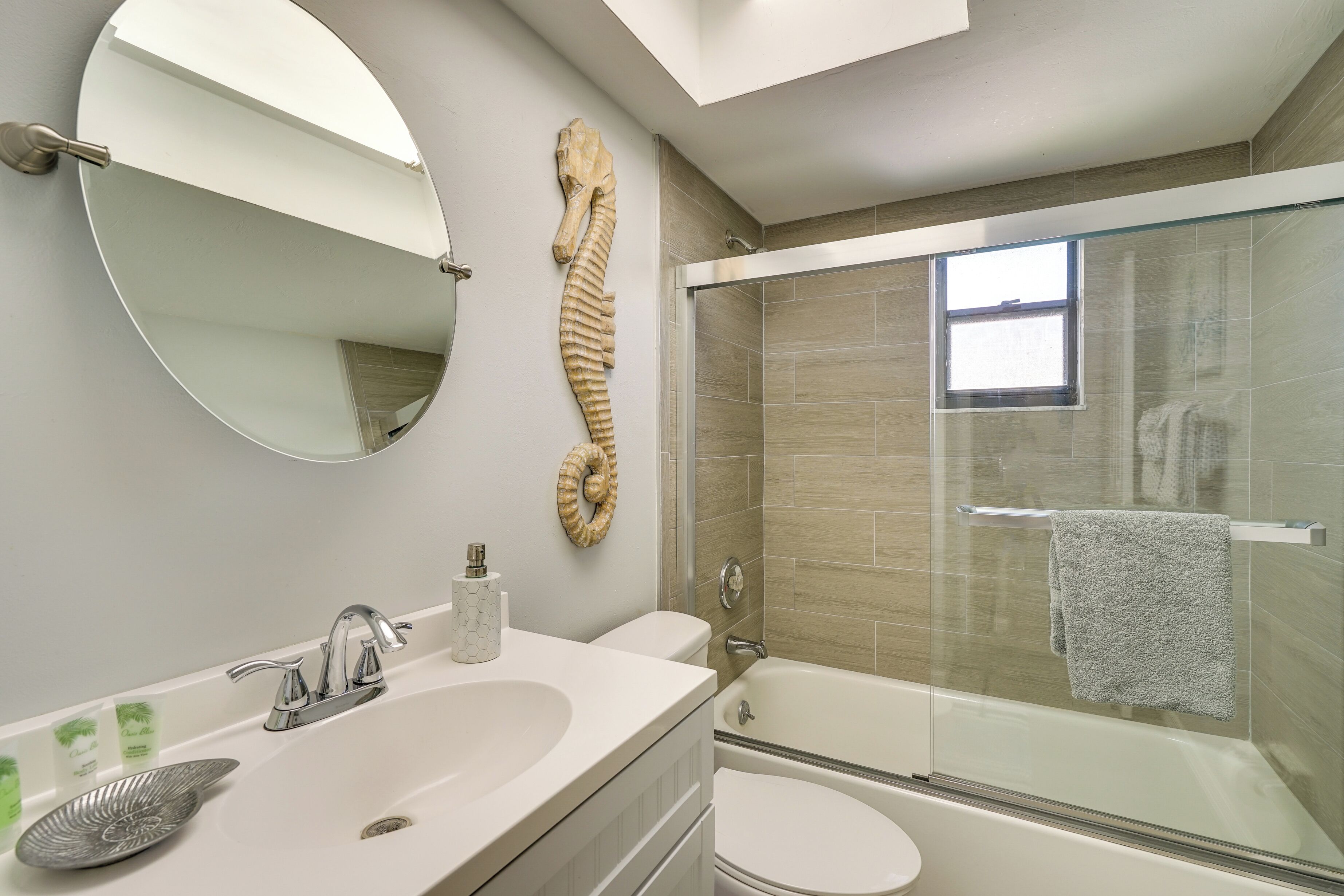 A modern bathroom with a large mirror, a round sink, a toilet, and a glass-enclosed shower area.