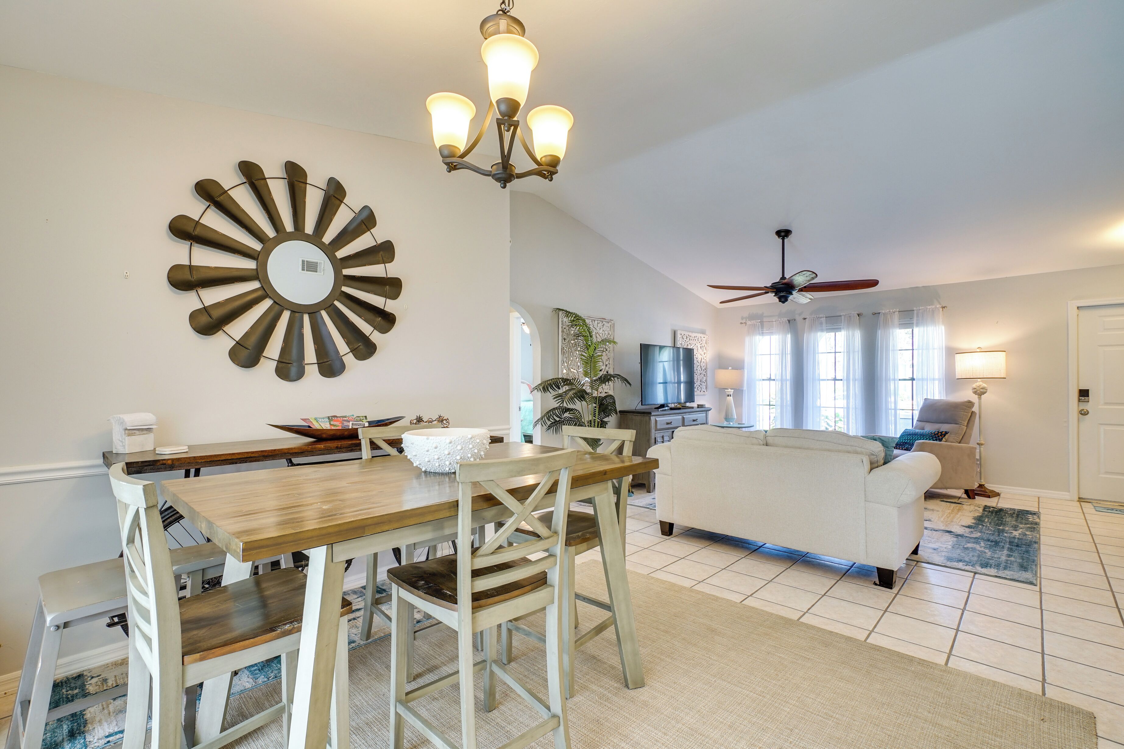 A dining area with a wooden table and chairs, a chandelier, and a large wall clock.