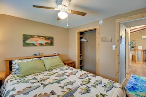 Un dormitorio con una cama decorada con un estampado de peces, un ventilador de techo y una puerta de madera que da al baño.