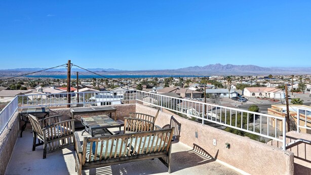 A rooftop terrace with outdoor furniture, a view of a residential area, and mountains in the distance.