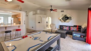 A living room with a foosball table, a sofa, a red curtain, and a ceiling fan.
