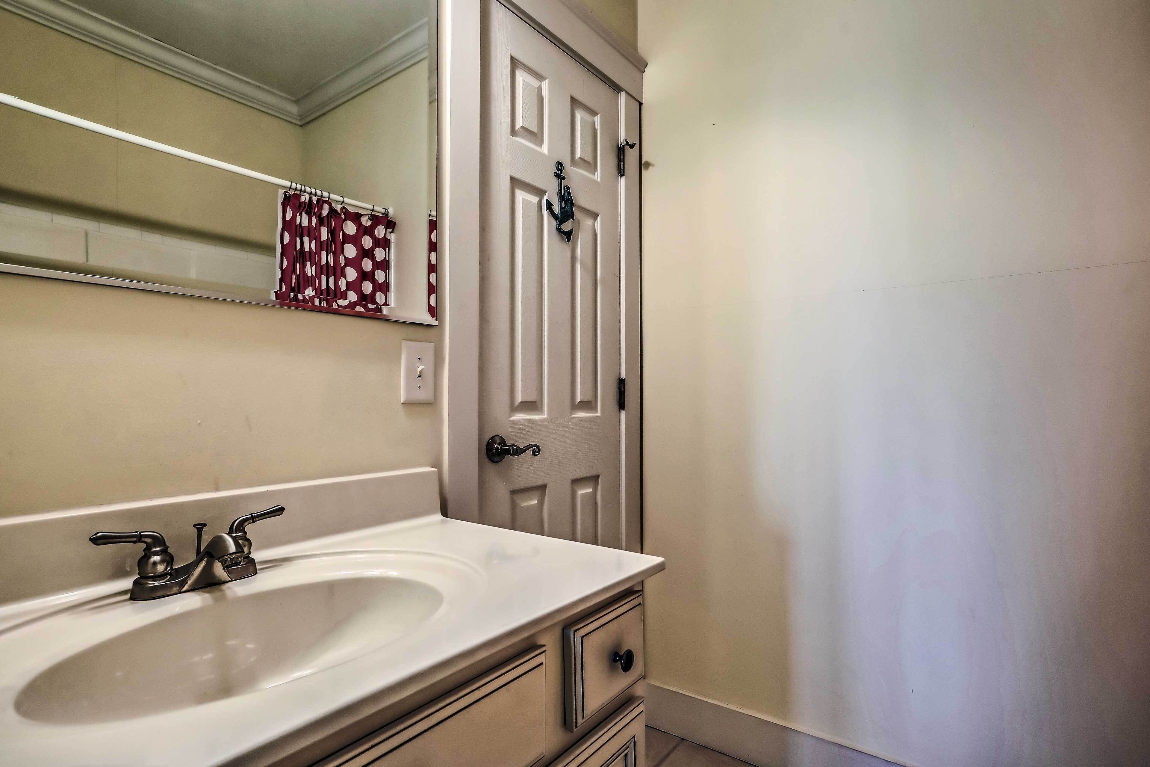 A bathroom with a white sink, a towel rack with a polka dot towel, and a door with an anchor decoration.