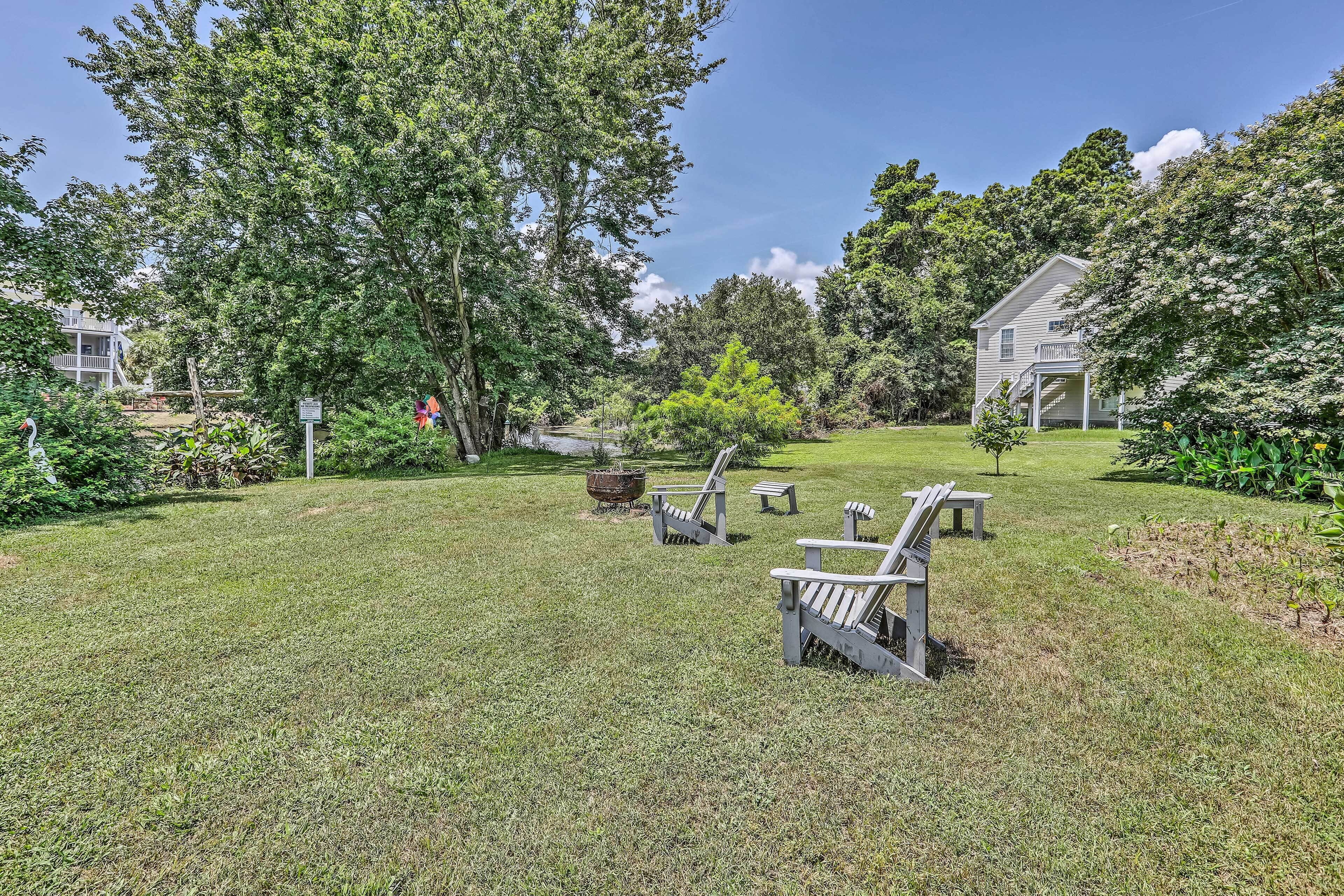 A grassy backyard with Adirondack chairs, a fire pit, and a small tree.