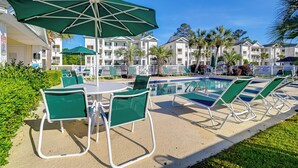 A poolside area with lounge chairs and umbrellas, surrounded by a white fence and palm trees. - Cozy Condo w/ Golf Course View: 4 Mi to Shore! (Myrtle Beach)