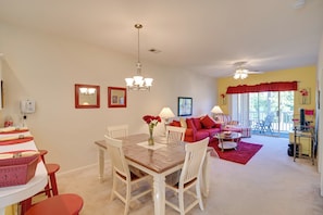 A dining area with a wooden table and white chairs, a chandelier, and a red rug.