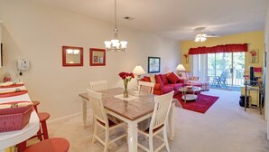 A dining area with a wooden table and white chairs, a chandelier, and a red rug. - Cozy Condo w/ Golf Course View: 4 Mi to Shore! (Myrtle Beach)