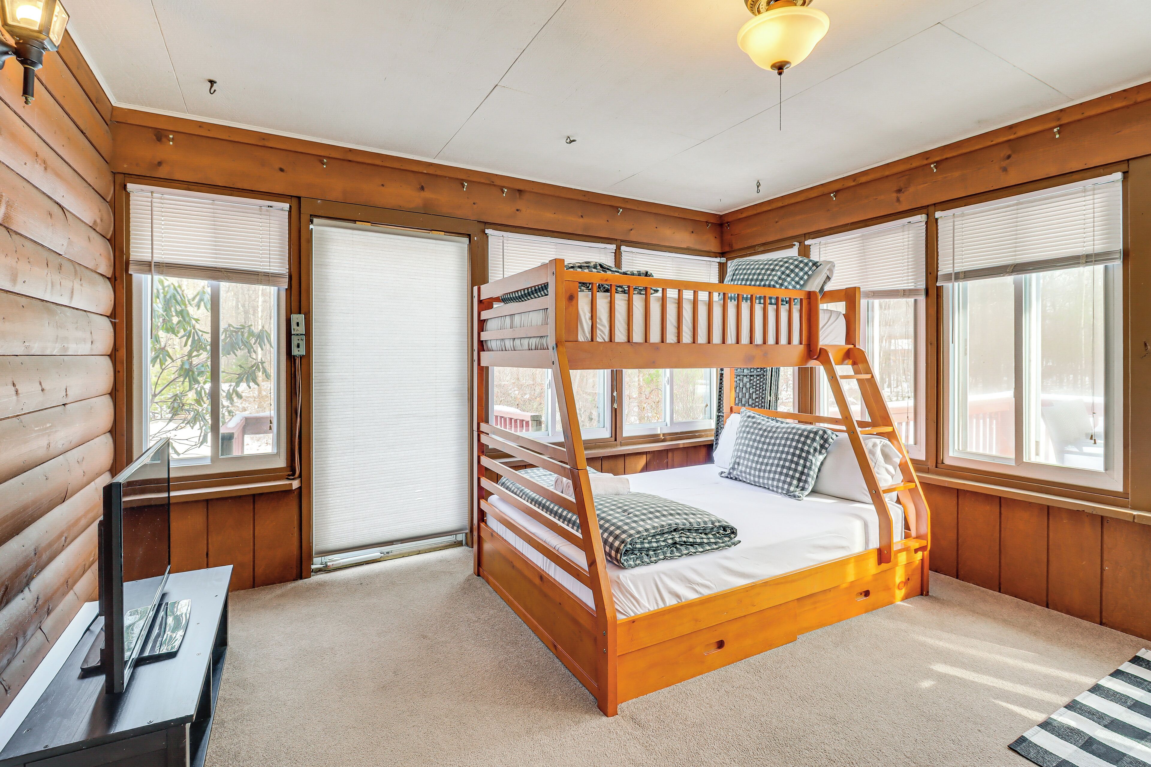 A bunk bed in a cabin-style room with wooden walls, large windows, and a ceiling light.