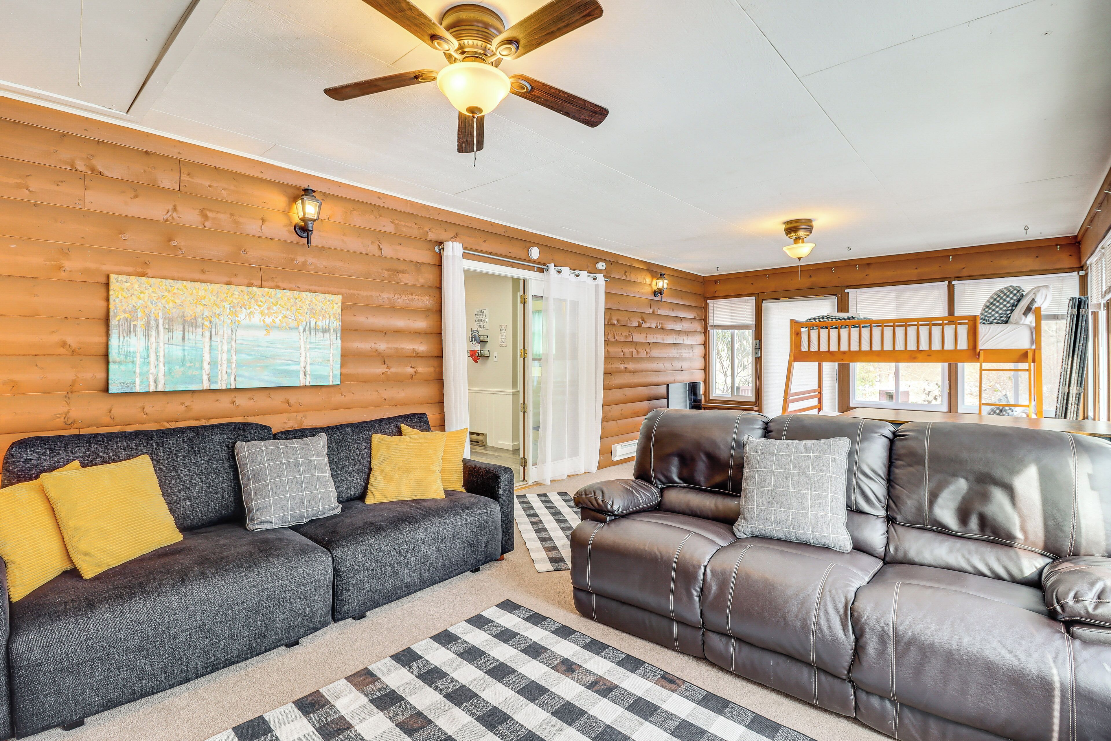 A cozy log cabin interior with a gray sofa, a leather recliner, and a wooden ceiling fan.