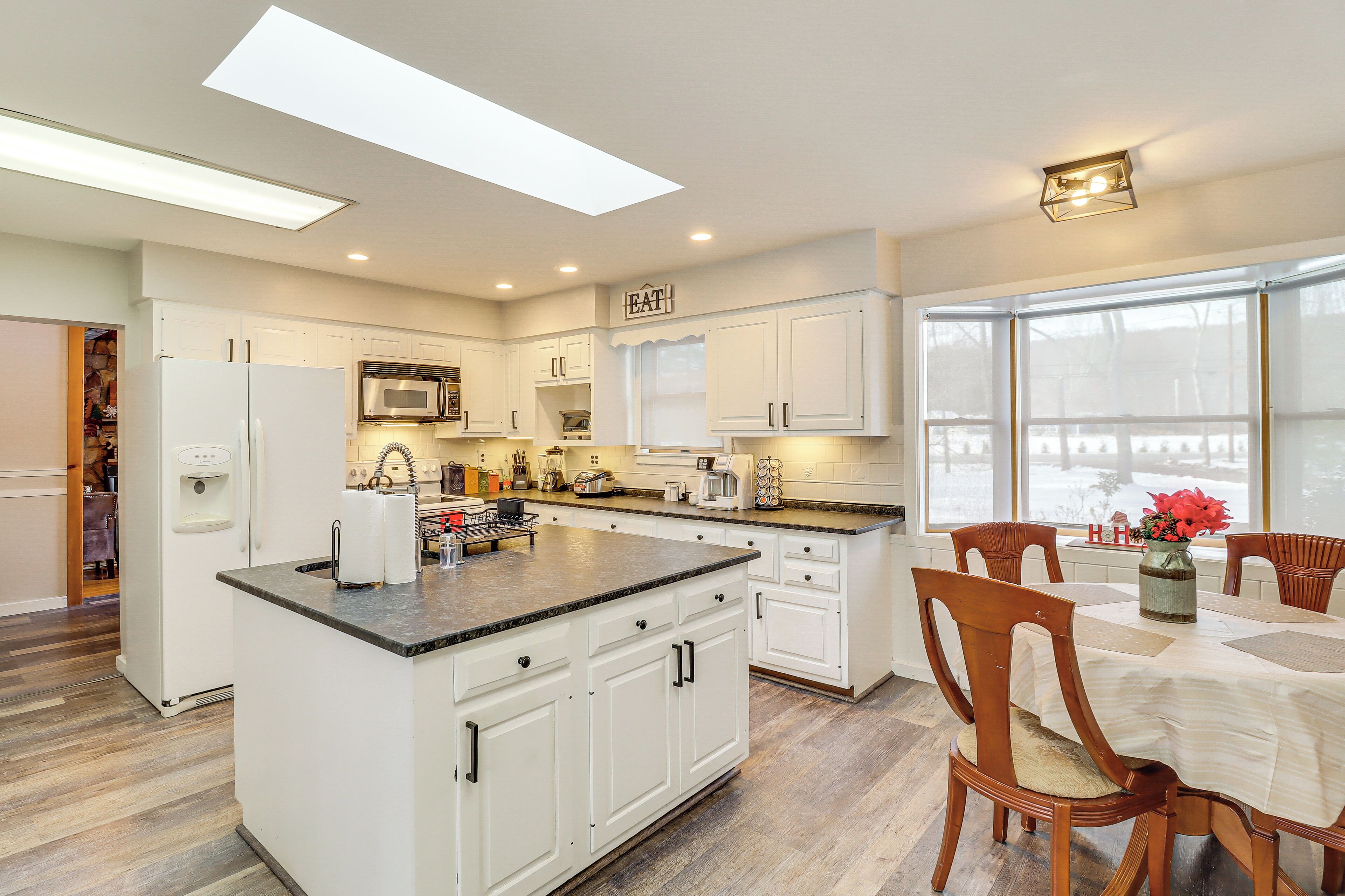 Una cocina moderna con armarios blancos, una isla central y un comedor con sillas de madera.