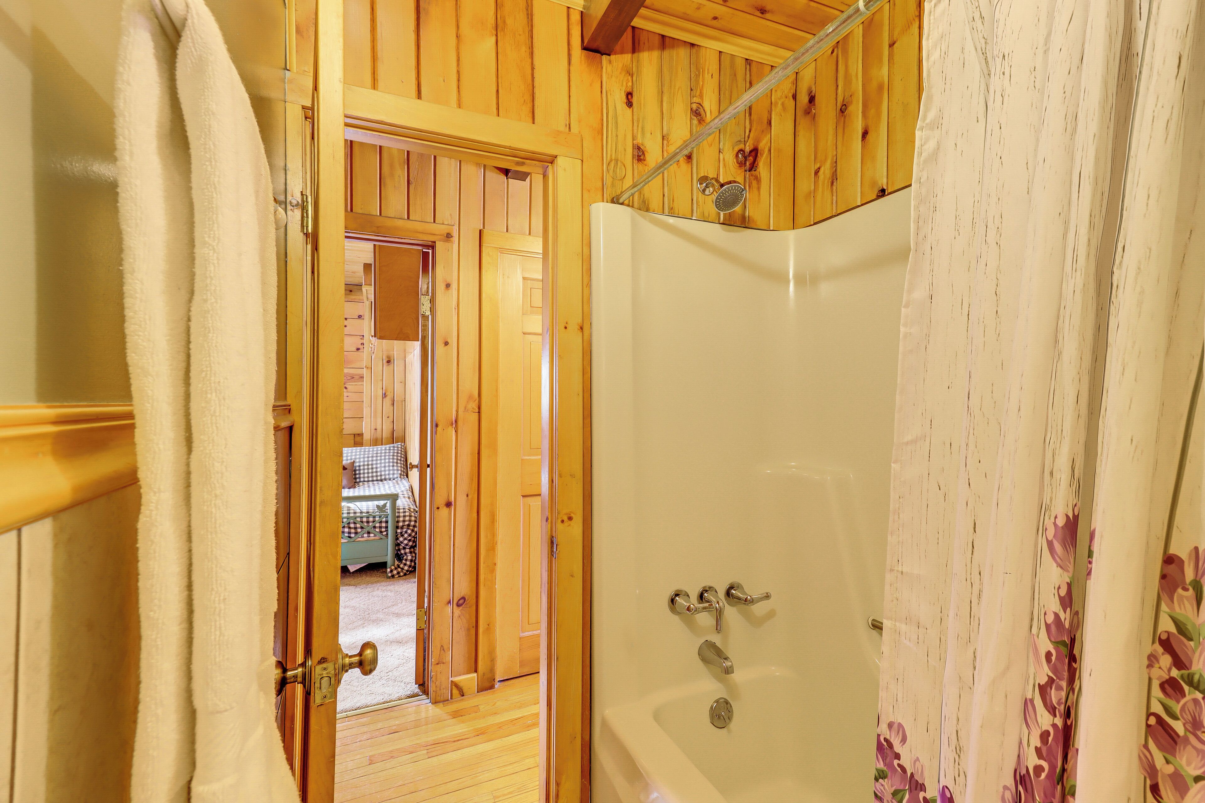 A wooden interior with a shower and a door leading to a room with a bed.
