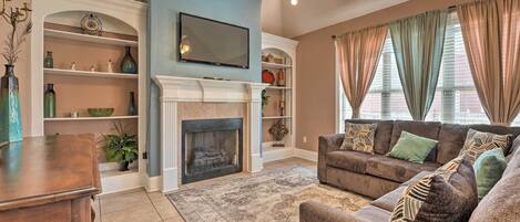 A living room with a fireplace, a television, a sofa, and a ceiling fan.