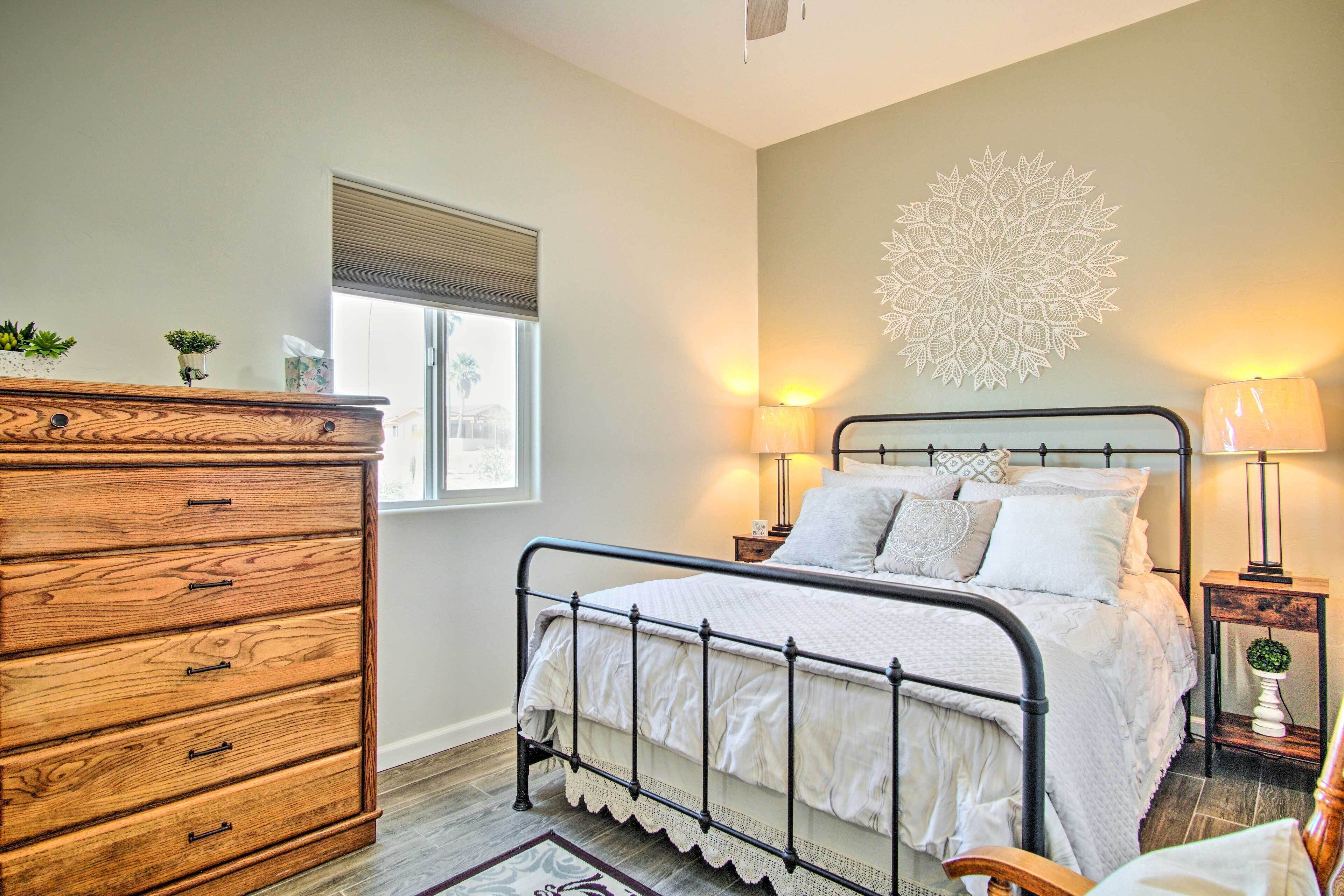A bedroom with a bed, dresser, bedside lamps, and a decorative wall piece.