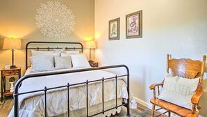 A neatly made bed with a headboard, two bedside lamps, a decorative wall piece, and a wooden chair with a cushion. - Tucson Vacation Rental ~ 5 Mi to Nat'l Park (Tucson)
