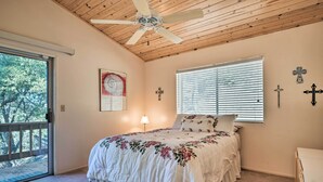 A bedroom with a wooden ceiling, a bed with floral bedding, a window with blinds, and a door leading to a balcony. - Pine Mountain Club Cottage W/wraparound Deck! (Pine Mountain Club)