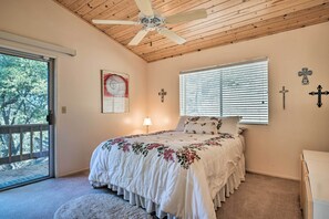 A bedroom with a wooden ceiling, a bed with floral bedding, a window with blinds, and a door leading to a balcony. - Pine Mountain Club Cottage W/wraparound Deck! (Pine Mountain Club)