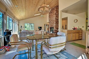 Ein geräumiges Wohnzimmer mit einer großen Holzbalkendecke, einem Kamin aus Backstein und einem Essbereich mit einem Glastisch und modernen Stühlen.