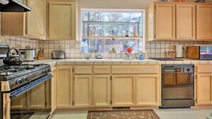 A kitchen with wooden cabinets, a stove, a dishwasher, and a window with a view of trees. - Pine Mountain Club Cottage W/wraparound Deck! (Pine Mountain Club)